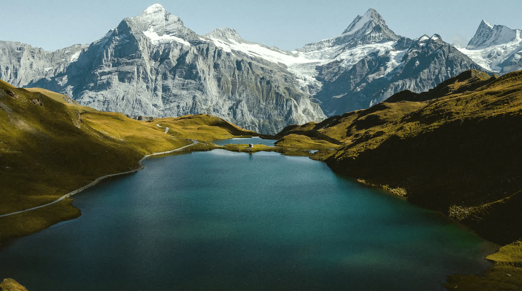 A turquoise alpine lake below snow-capped peaks in the Swiss Alps.