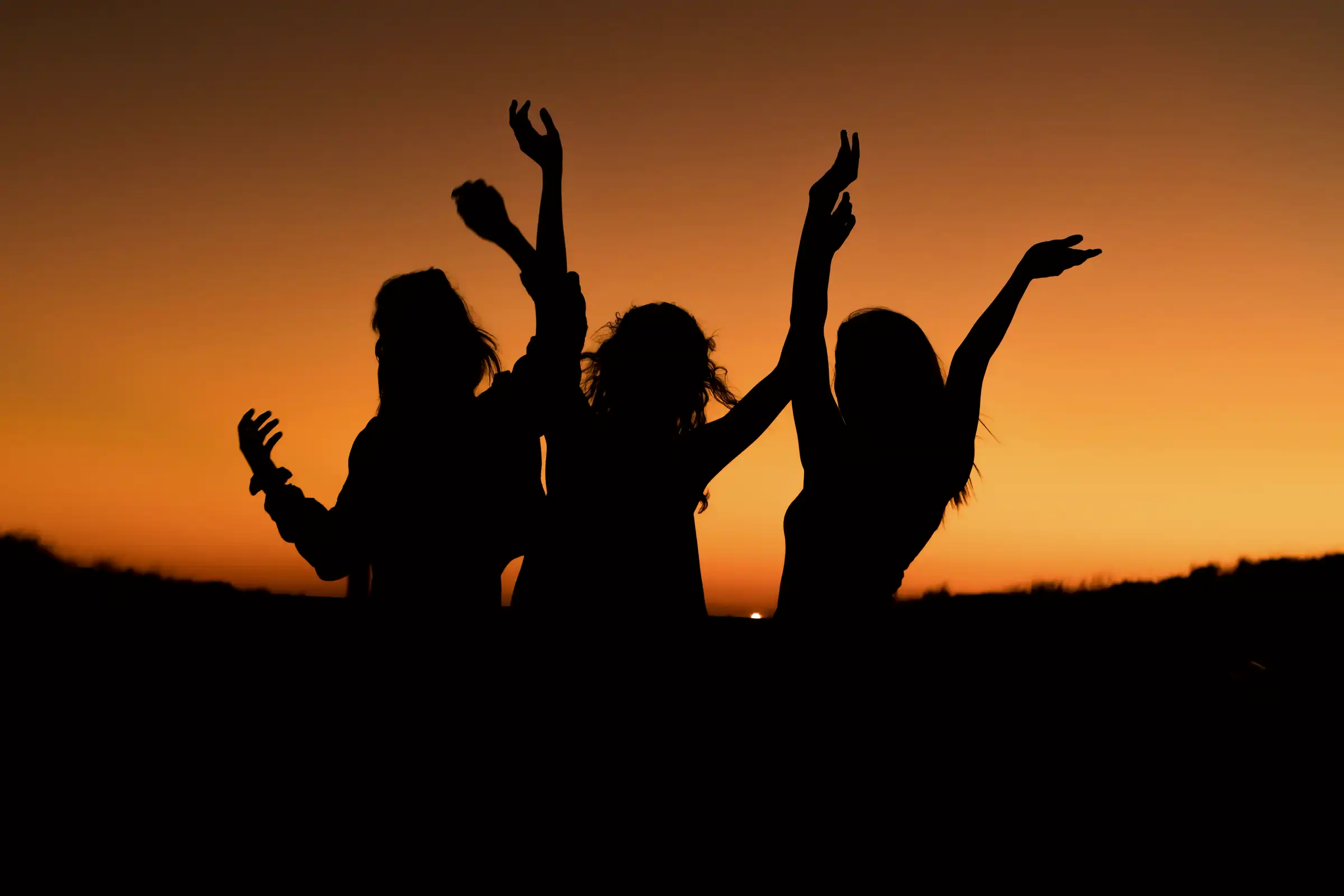 Three friends dancing in silhouette against a sunset.