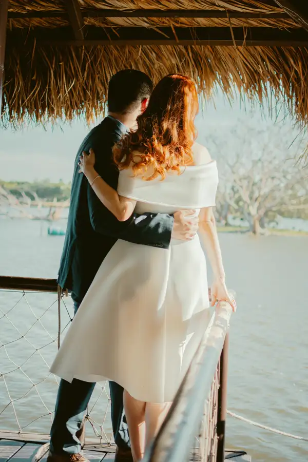 A couple embracing on a jetty, looking out over the water.